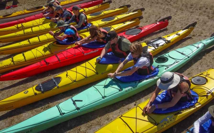 outward bound students sit in beached kayaks, practicing their skills